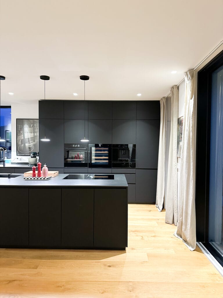 Moderne, schwarze Küche mit Insel einegbauten Geräten in offener Atmosphäre.