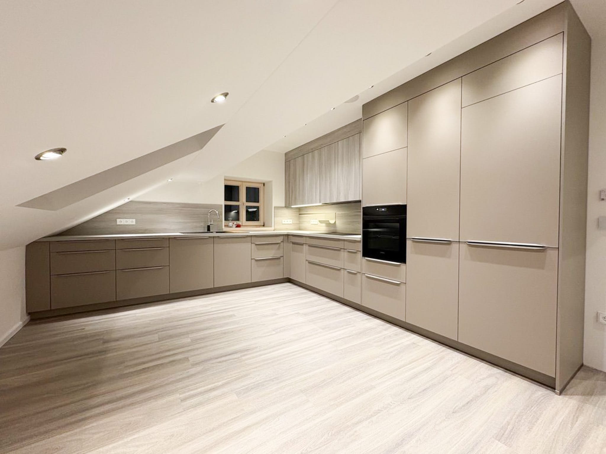 Moderne Küche unter der Dachschräge in neutralen Tönen. (mit minimalistischen Griffen und gut integrierten Geräten.)