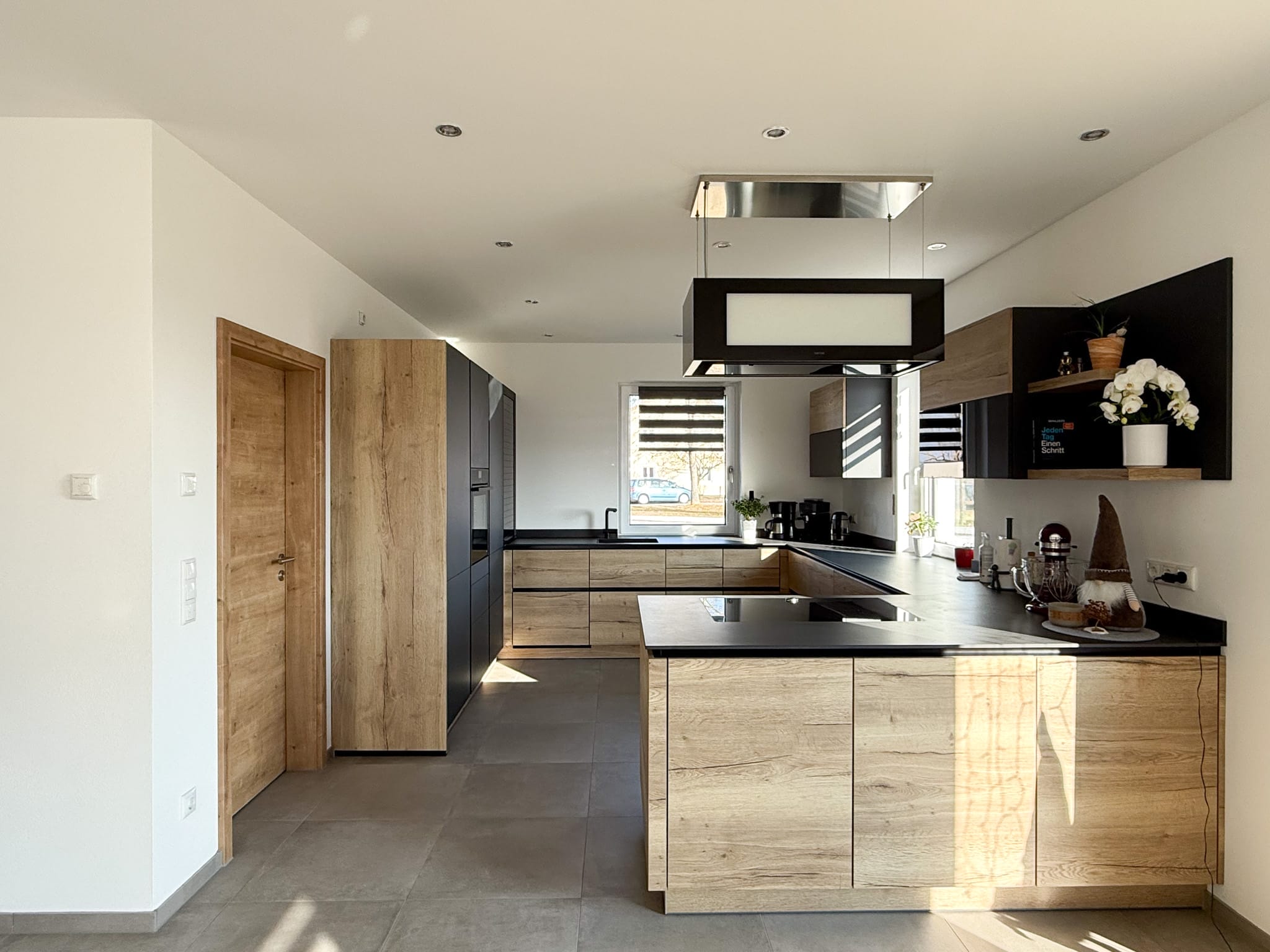 Offene Holzküche mit schwarzen Akzenten und Kochinsel mit Dunstabzug.