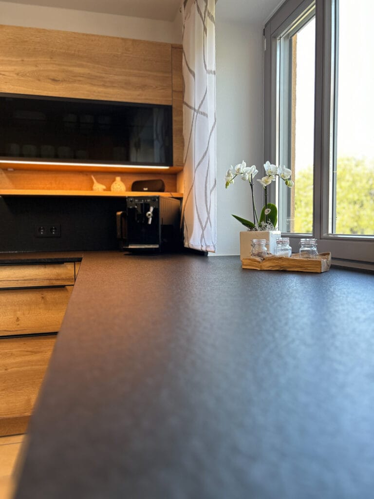 Holzküche mit dunkler Arbeitsplatte im Fokus, darauf Orchideen als Dekoration.