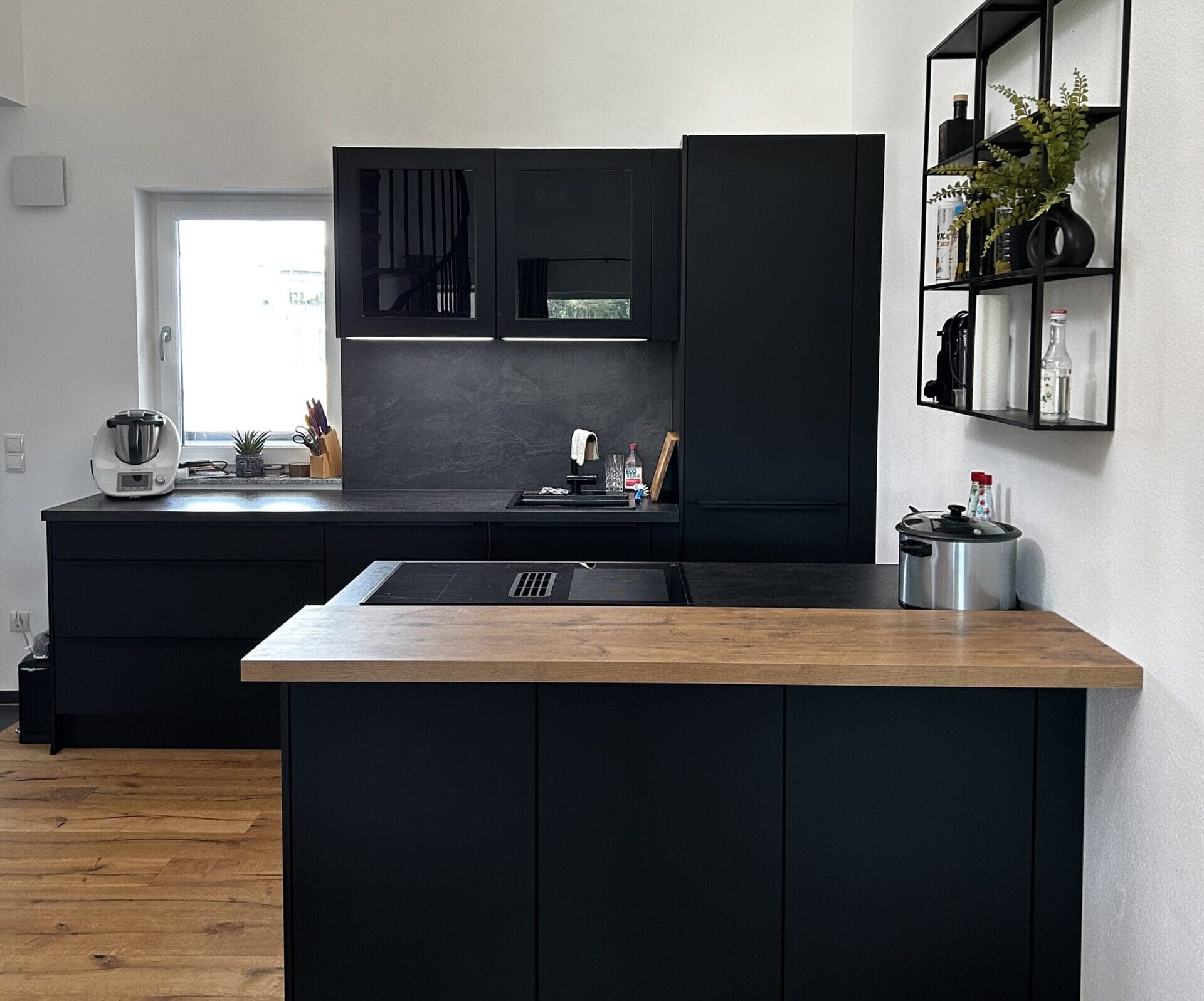Schwarze Küche mit Holzdetails und -boden.