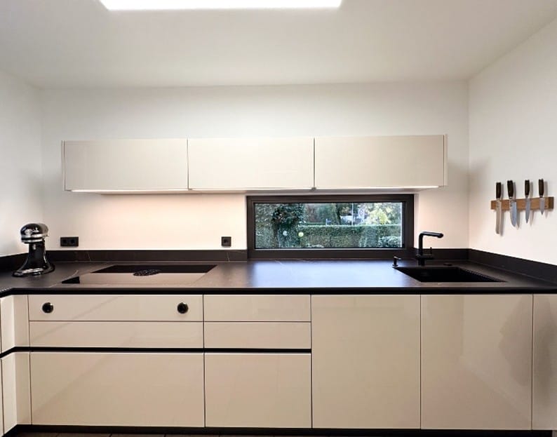 Moderne Küche mit hochglänzenden, cremeweißen Fronten, schwarzer Arbeitsplatte