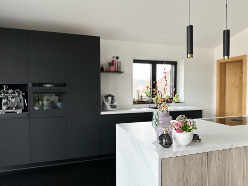 Moderne Küche mit mattschwarzen Fronten, heller Arbeitsplatte und Kochinsel in Holzoptik.